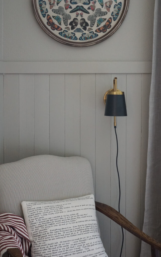 A black plug-in sconce over a chair next to a shiplap wall.